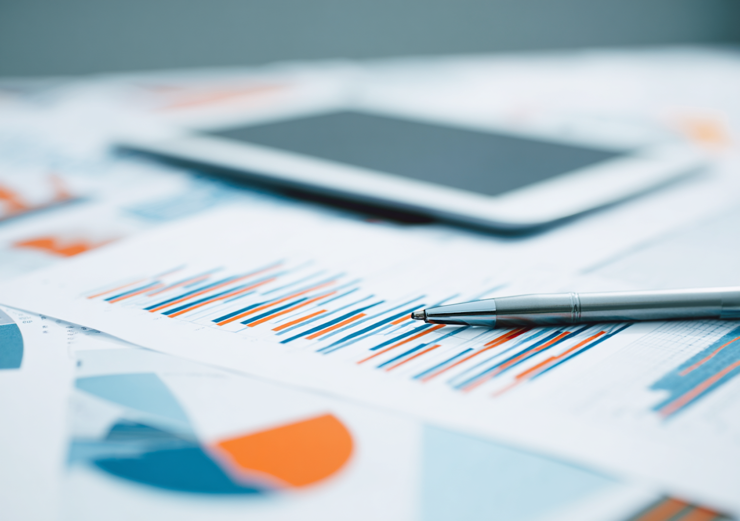 Financial charts, a pen, and a tablet on a desk